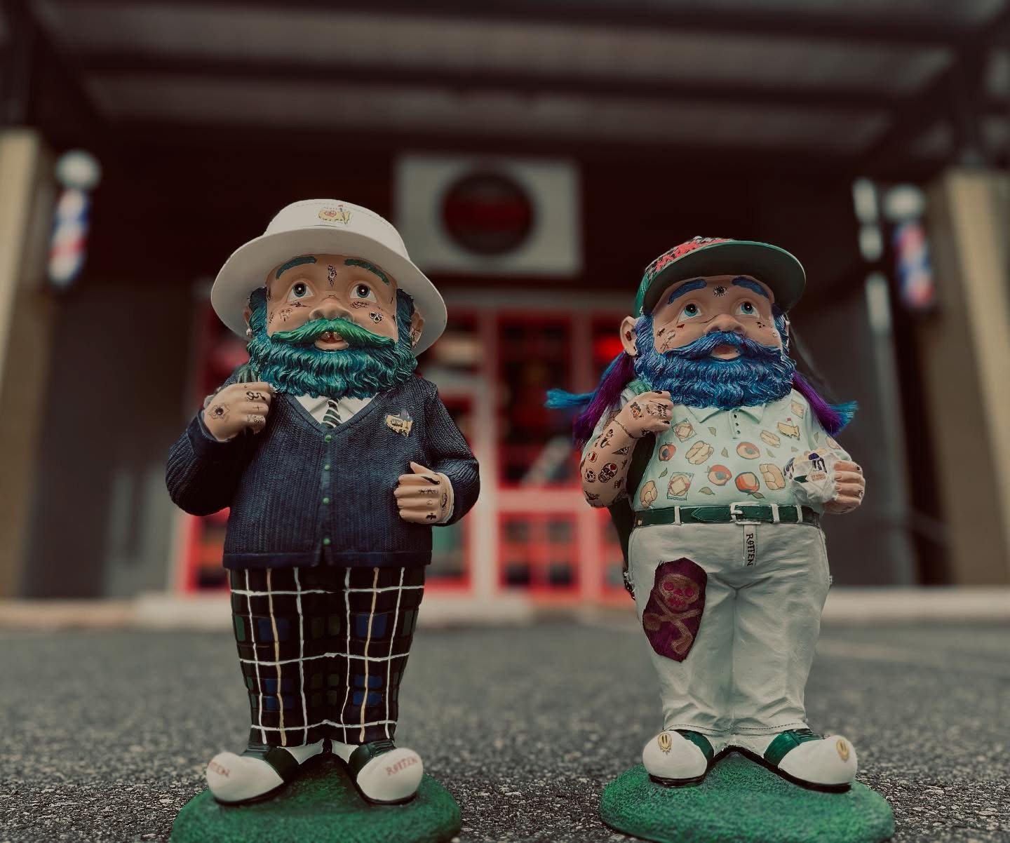 Two garden gnomes with long beards standing on the pavement in front of the shop.